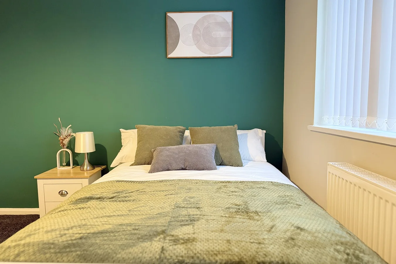 Well-furnished bedroom with a green feature wall, neatly made bed and natural light