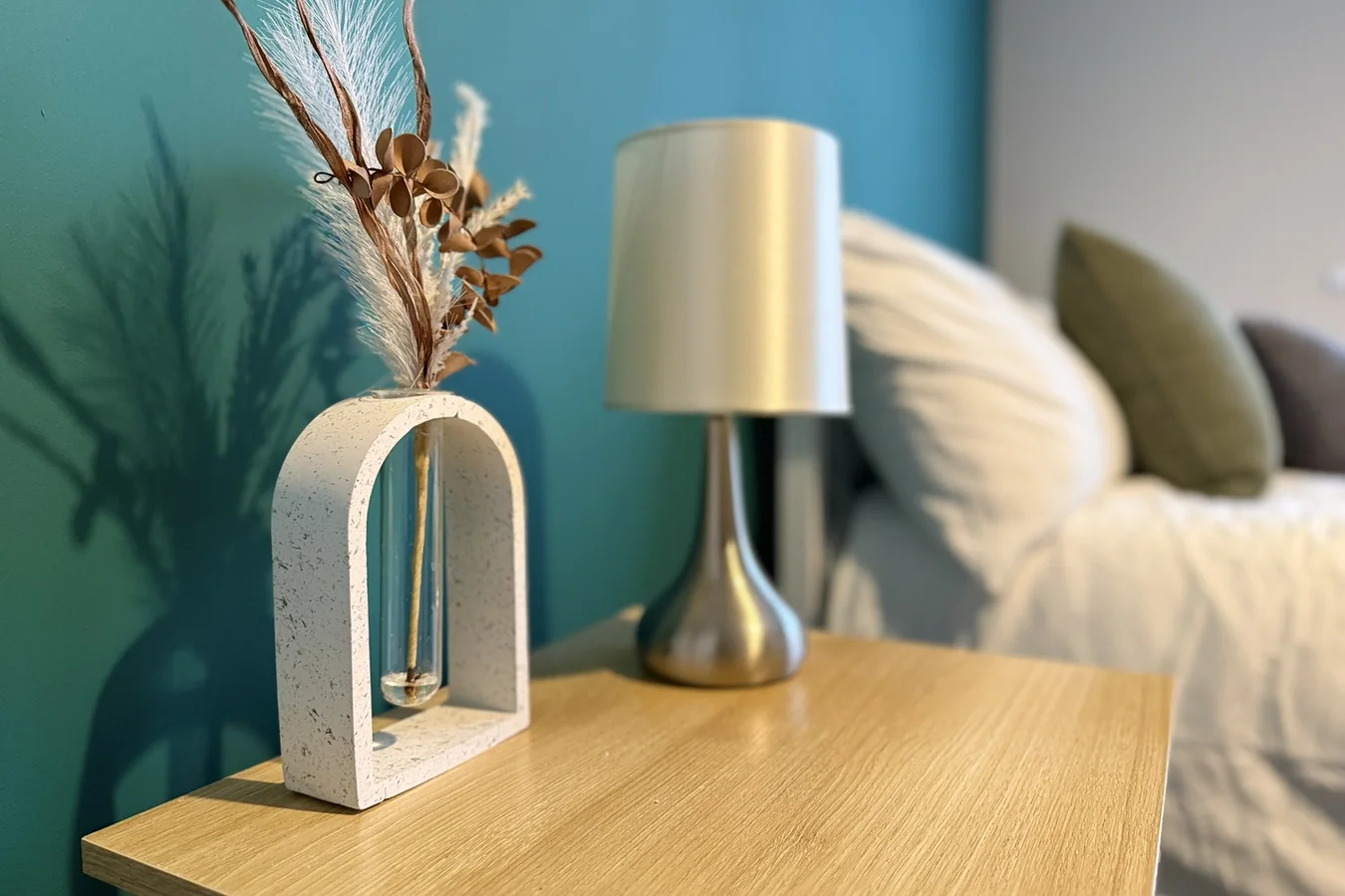 Bedside table with decorative flowers and a lamp beside a furnished bed